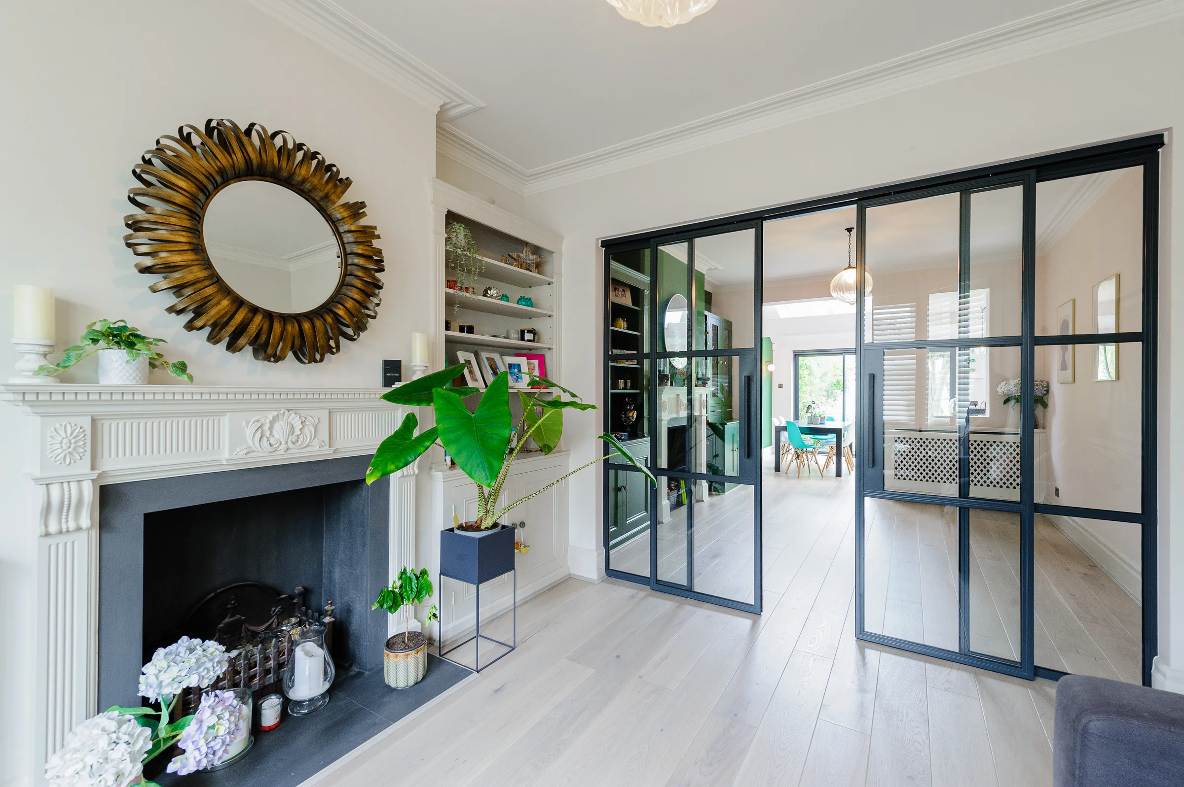 Period living room with a white marble fireplace and gilded mirror, opening through steel-framed glass doors to the dining room