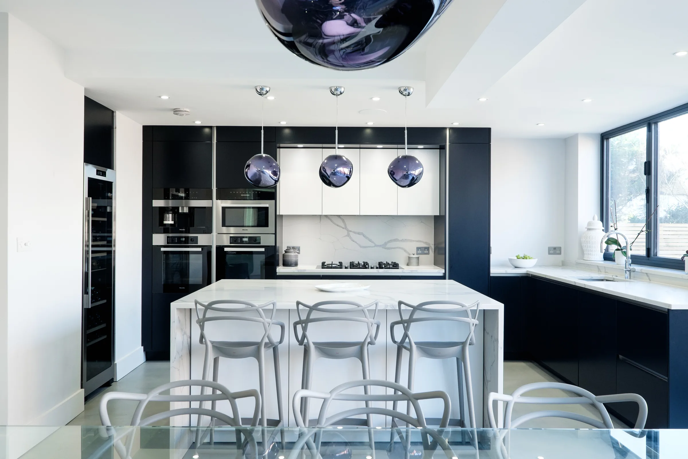 Navy and white kitchen with a marble island, bar stools and statement pendant lights