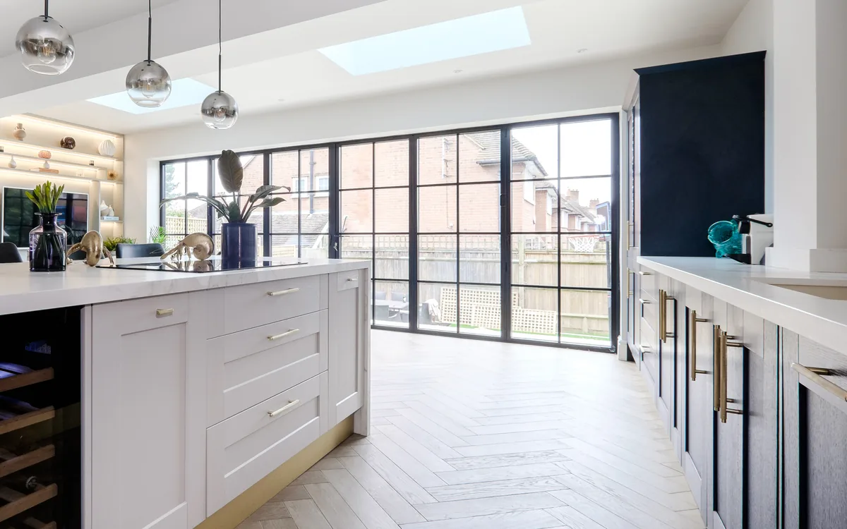 Open-plan kitchen extension with a marble-topped island, herringbone oak floor, rooflights and black-framed glazed doors to the garden
